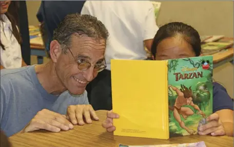  ?? WILLIAM ROLLER PHOTO ?? Bob Holzman (left), sixth-grade teacher at Desert Garden Elementary School during the book giveaway, organized by the Kiwanis Club of Early Risers and the Salvation Army explaining the book selection process to second-grade students in El Centro on...