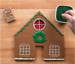  ??  ?? Zimmerman uses green-colored royal icing and green sprinkles to create a wreath as she decorates a gingerbrea­d house.