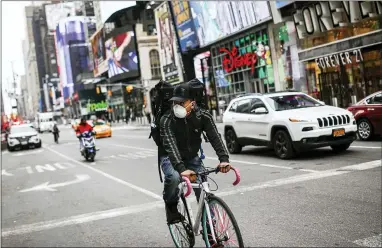  ?? JOHN MINCHILLO — THE ASSOCIATED PRESS ?? A bicycle delivery worker wears a protective face mask as he rides through a sparsely populated Times Square due to COVID-19concerns Friday in New York. New York Gov. Andrew Cuomo is ordering all workers in non-essential businesses to stay home.