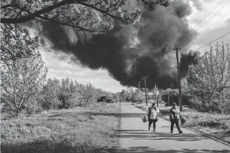  ?? MAURICIO LIMA NYT ?? Villagers on April 19 carry floral bouquets on a road near Kherson, Ukraine, as a huge plume of smoke rises from a factory hit by Russian shelling. Ukraine’s allies have invoked a sense of urgency over weapon deliveries, but Ukraine has little time to lose.