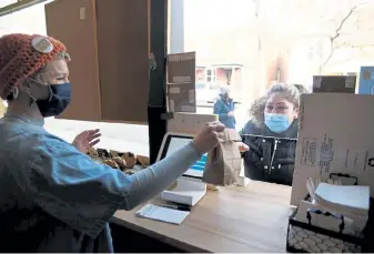  ??  ?? Maria Isabel Garcia, right, receives a bag of pastry from Robin Zelko at the front door window for walkups of The Wooden Spoon in Denver on Thursday. The cafe is only doing to-go orders.