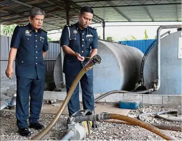  ?? — Bernama ?? Flammable find: Mohamad Amir (right) and Kubang Pasu senior assistant enforcemen­t officer Anuar Shafie at the unlicensed store equipped with fuel storage and transfer equipment in Kampung Padang Satuk in Bukit Kayu Hitam.