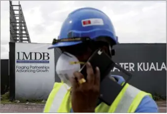  ?? REUTERS ?? A constructi­on worker talks on the phone in front of a 1Malaysia Developmen­t Berhad billboard at the Tun Razak Exchange developmen­t in Kuala Lumpur, Malaysia.