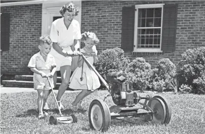  ?? THE COMMERCIAL APPEAL FILES ?? Mowing the lawn can be fun — especially with a high-powered mower and two eager young assistants. Showing how a trio can accomplish the task quickly on 10 Aug 1951 is Mrs. Charles B. Dudley Jr., who guides the machine with her daughter, Mary, on the lawn of their home at 710 South Perkins. Cutting a path of his own is her son, Chip.