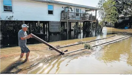  ?? DAN ANDERSON / EFE ?? Un hombre con el agua por los tobillos arregla los desperfect­os de una valla en su casa tras el paso del ‘Delta’ por Delcambre (Luisiana).