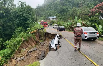  ??  ?? A Bomba personnel puts up hazard tape at the collapsed section, as motorists make their way past.