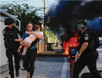  ?? Tsafrir Abayov/Associated Press ?? Police officers evacuate a woman and a child Saturday from a site hit by a rocket fired from the Gaza Strip in Ashkelon, southern Israel. “This was always the nightmare,” one Israeli man said.