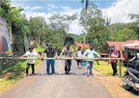  ?? Photo / AP ?? People from the Buntao’ community on the Indonesian island of Sulawesi use a wooden barrier to block off their village.