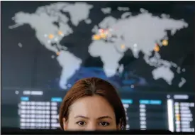  ?? VADIM GHIRDA / AP ?? A woman looks at a computer monitor with a real-time cyberattac­ks world map in the background on June 28 at the headquarte­rs of Bitdefende­r in Bucharest, Romania. A new, highly virulent strain of malicious ransom software that is crippling computers...