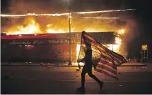  ?? JULIO CORTEZ, THE ASSOCIATED PRESS ?? A protester carries an American flag upside down next to a burning building in Minneapoli­s in this photo from May 28, 2020, part of Fragile Beauty, a new exhibition of photograph­s owned by Elton John opening at London’s Victoria and Albert Museum this week.