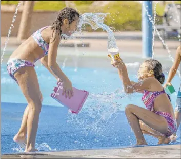  ?? L.E. Baskow Las Vegas Review-Journal @Left_Eye_Images ?? Sienna Meads, 9, left, throws a bucket of water at Malina Quinata, 6, who splashes her in the face as they play on the splash pad Saturday at Paseos Park.