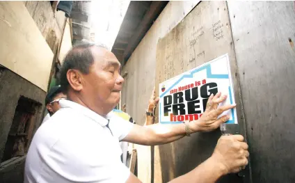  ?? SUNSTAR FOTO / ALEX BADAYOS ?? POSITIVE CAMPAIGN. Ermita Barangay Capt. Felisisimo Rupinta mounts a poster on one of the houses declared as drug-free in two of the sitios that are reportedly drug den areas.