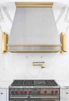  ?? JENNIFER BACKSTEIN INTERIORS ?? JBI created this custom range hood with brushed metal and bands
of matte brass to mesh with the sconces that flank the range.