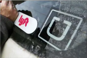  ?? GENE J. PUSKAR — THE ASSOCIATED PRESS FILE ?? FILE- In this file photo, a Lyft logo is installed on a Lyft driver’s car next to an Uber sticker in Pittsburgh.