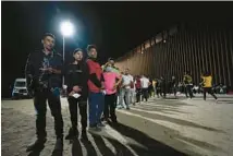  ?? GREGORY BULL/AP ?? Migrants wait along a border wall on Tuesday after crossing from Mexico near Yuma, Arizona.