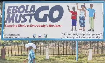  ?? AFP ?? A man walking past an Ebola campaign banner with the new slogan “Ebola Must GO” in Monrovia, Guinea.