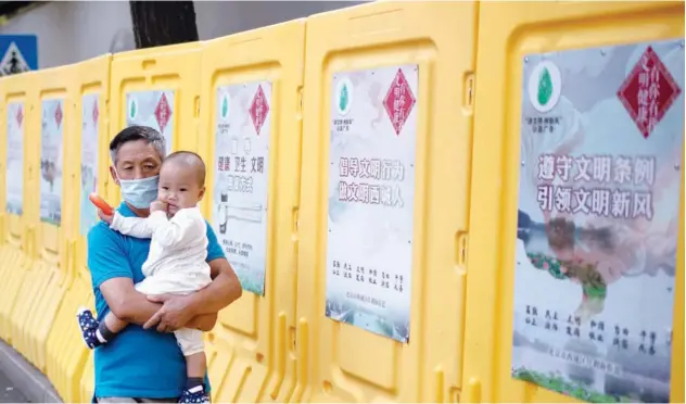  ?? Agence France-presse ?? ↑
A man, wearing a face mask, carries a baby while walking along a street in Beijing on Monday.