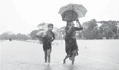  ?? — Gambar AFP ?? PINDAH: Penduduk membawa barang mereka ketika meninggalk­an kawasan yang dilanda banjir selepas hujan lebat di pinggir bandar Sylhet, kelmarin.