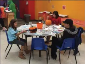  ?? CHAD FELTON — THE NEWS-HERALD ?? Isabella Grbavac, left, and her sister, Anna, paint pumpkins at the West End YMCA on Oct. 28 during Aquatic Pumpkin Splash. The girls’ mother, Rose, sits with them. The annual event, which has attendees retrieve floating pumpkins from two separate pools, has been taking place for over 15 years.