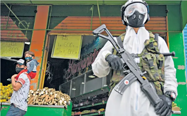  ??  ?? Passers-by eye a masked soldier as he enforces a strict lockdown in Bogota which has seen a spike in Covid-19 cases