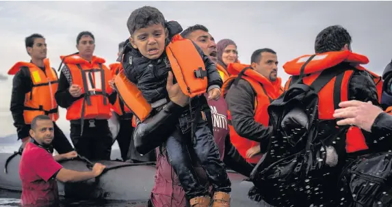  ?? Santi Palacios ?? > Volunteers assist refugees from a dinghy after they crossed a part of the Aegean sea from Turkey to the Greek island of Lesbos in 2015