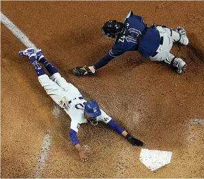  ?? AP Photo/David J. Phillip ?? ■ Los Angeles Dodgers' Mookie Betts scores past Tampa Bay Rays catcher Mike Zunino on a fielders choice by Max Muncy during the fifth inning in Game 1 of the baseball World Series Tuesday in Arlington, Texas.