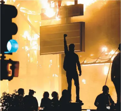  ?? JULIO CORTEZ/AP ?? A protester stands on a platform in front of a fire at a restaurant early Friday in Minneapoli­s. Protests over the death of George Floyd, a black man who died in police custody Monday, broke out in Minneapoli­s for a third straight night.