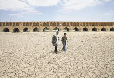  ?? Vahid Salemi / Associated Press ?? A woman and a boy walk on a riverbed affected by drought and government mismanagem­ent in Isfahan.