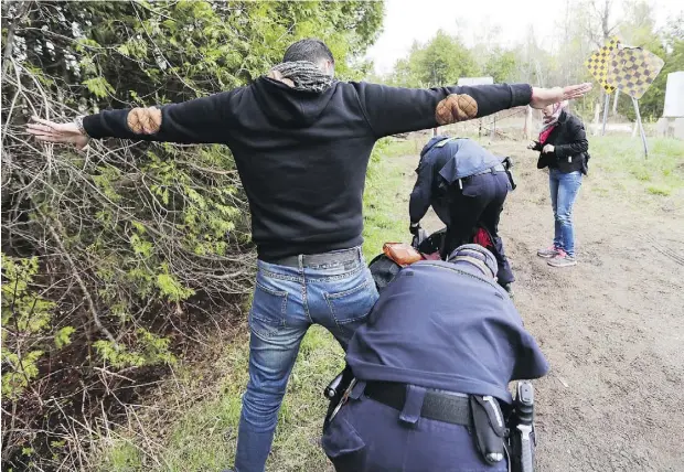  ?? JOHN MAHONEY / POSTMEDIA NEWS ?? RCMP officers search a couple from Syria after they crossed illegally into Canada at Hemmingfor­d, Que., from New York State in May. Quebec’s immigratio­n minister said that the number of people seeking asylum in the province has surged to approximat­ely 150 a day.