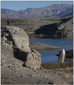  ?? (AP/John Locher) ?? A man stands on a hill overlookin­g a boat left standing upright with its stern buried in the mud in Lake Mead at the Lake Mead National Recreation Area near Boulder City, Nev.