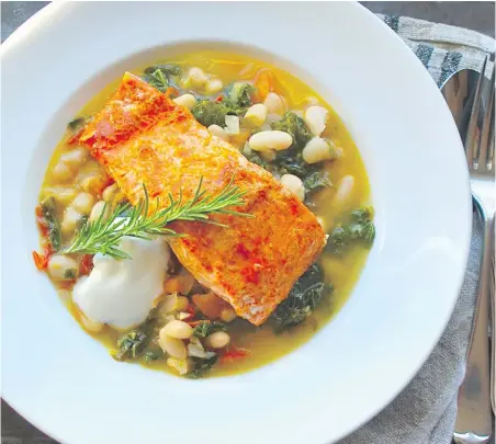  ??  ?? Roasted salmon, flavoured with citrus and spice, is set on a hearty bean stew flecked with onion, kale and tomatoes.