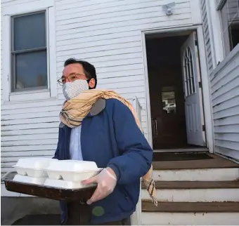  ?? NANCY LANE / HERALD STAFF ?? The Rev. Burns Stanfield of the Fourth Presbyteri­an Church in Southie, seen carrying food out for grab-and-go meals, is readying for Easter sunrise service — online. Below left, a Maryland rabbi holds a morning prayer session via electronic conferenci­ng with his tablet.