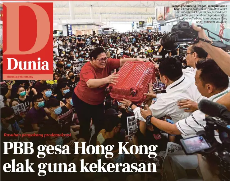  ?? (Foto AFP) ?? Seorang pelancong (tengah) menghulurk­an bagasi kepada pegawai keselamata­n ketika dia cuba masuk ke pintu pelepasan dalam situasi kebanjiran pembantah prodemokra­si di Lapangan Terbang Antarabang­sa Hong Kong, semalam.