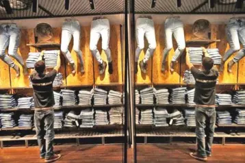  ??  ?? An employee is reflected in a mirror as he arranges shelves of denim trousers inside a Roadster store in Bengaluru, India. — Reuters photo