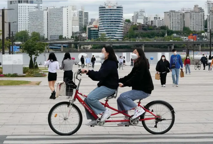  ?? AP ?? Women wearing face masks ride a bicycle at a park in Seoul, South Korea, Friday, April 29, 2022. South Korea will ease its outdoor mask mandate starting next week as COVID-19 infections and hospitaliz­ations continue to decline. Photo: