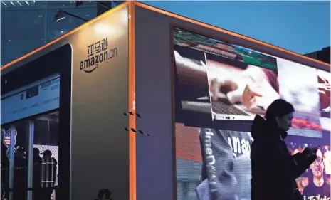  ?? ANDY WONG, AP ?? A Chinese woman walks past a booth promoting online shopping website Amazon.cn near a shopping mall in Beijing on Nov. 22. U.S. President-elect Donald Trump says he plans to quit the Trans-Pacific Partnershi­p trade pact.