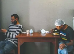  ??  ?? Bhadel (left) uses his phone as his taxi driver friend Indra Kumar Newar eats his lunch before delivering food at the teaching hospital. The two friends have taken their own money and donations and put it to use buying groceries, renting a kitchen and paying helpers to provide the meals.