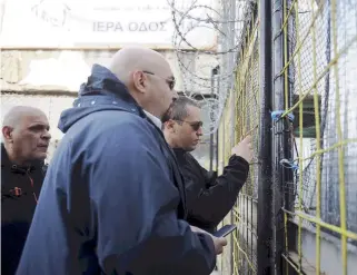  ??  ?? Golden Dawn spokesman Ilias Kasidiaris (right) and MP Ilias Panagiotar­os (center) peer through the gates of the site slated for Athens’s first mosque following a police raid yesterday that removed nationalis­t squatters from the premises.