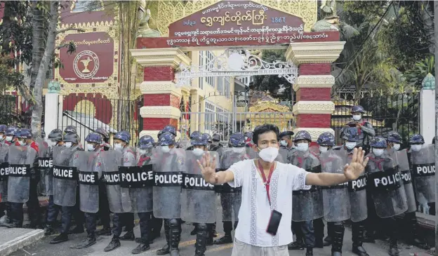  ??  ?? 0 A man gestures as police stand guard at the entrance gate of a Buddhist monastery where pro-military supporters took shelter after clashes with residents