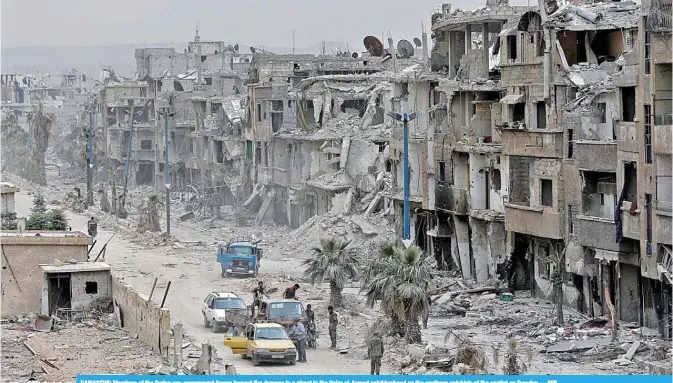  ??  ?? DAMASCUS: Members of the Syrian pro-government forces inspect the damage in a street in the Hajar al-Aswad neighborho­od on the southern outskirts of the capital on Tuesday. —AFP