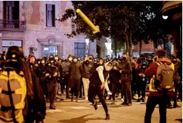  ?? — AP ?? A man throws a road sign against police officers protecting a national police station during clashes following a protest condemning the arrest of rap singer Pablo Hasél in Barcelona, on Sunday.