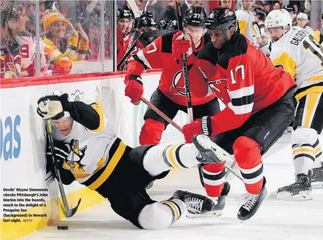  ?? GETTY ?? Devils’ Wayne Simmonds checks Pittsburgh’s John Marino into the boards, much to the delight of a Penguins fan (background) in Newark last night.