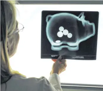  ?? FOTO: DPA ?? Eine Radiologin hält in ihrer Praxis in München (Oberbayern) eine Röntgenauf­nahme eines Sparschwei­ns gegen einen Leuchtkast­en: Neue Richtlinie­n verpflicht­en Banken und Sparkassen zu mehr Kostentran­sparenz.