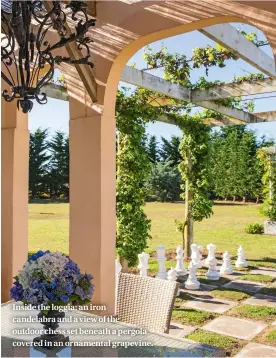  ??  ?? Inside the loggia: an iron candelabra and a view of the outdoor chess set beneath a pergola covered in an ornamental grapevine.