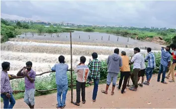  ?? — P. SURENDRA ?? Top: People watch the flow of flood water at Kapra lake on Saturday. Bottom: The flood water washed away a road at Sadhana Vihar Colony, where a house collapse too was reported.