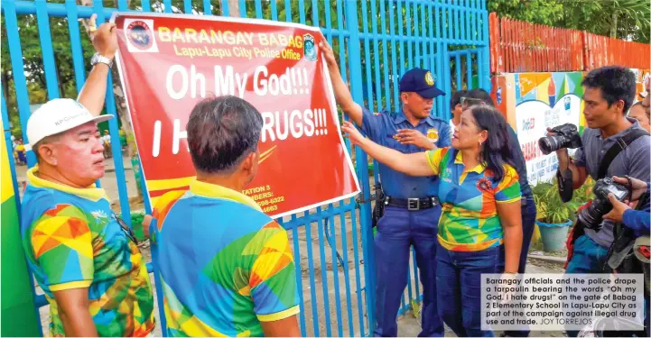  ?? JOY TORREJOS ?? Barangay officials and the police drape a tarpaulin bearing the words “Oh my God. I hate drugs!” on the gate of Babag 2 Elementary School in Lapu-Lapu City as part of the campaign against illegal drug use and trade.