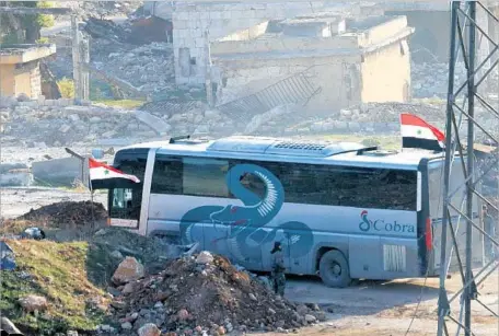  ?? George Ourfalian AFP/Getty Images ?? A BUS DRIVES through a Syrian government-controlled crossing on the southern outskirts of Aleppo during an operation to evacuate rebel fighters and civilians from opposition-held areas. The evacuation temporaril­y stalled after gunmen set fire to some...