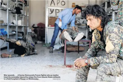  ?? PHOTO: REUTERS ?? War wounds . . . A Syrian Democratic Forces fighter sits as medics treat his comrades injured by sniper fire from Islamic State militants in a field hospital in Raqqa on Wednesday.