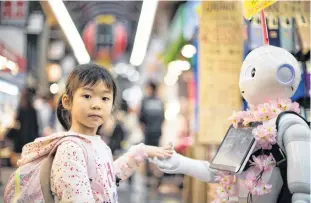  ?? ANDY KELLY • UNSPLASH ?? Computer-brain interfaces are no longer science fiction. Here, a girl interacts with a robot at Kuromon Market in Osaka.