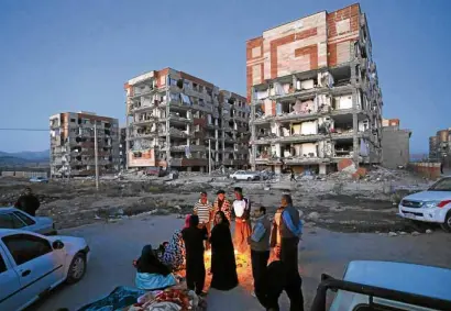  ?? —AP ?? Quake survivors in the Iranian city of Sarpol-e-Zahab warm themselves outside following the 7.3-magnitude quake that killed more than 100 in their city alone.